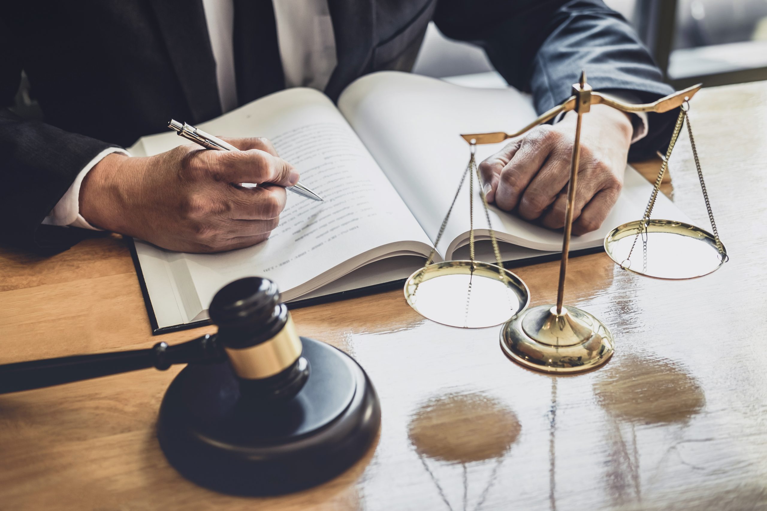 lawyer writing in book with gavel and scales of justice in front of him
