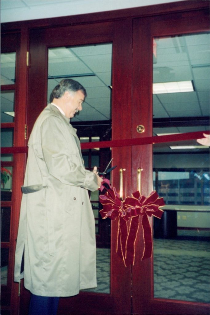 Jim Roe holding a pair of scissors cuts a rubbon to the new office