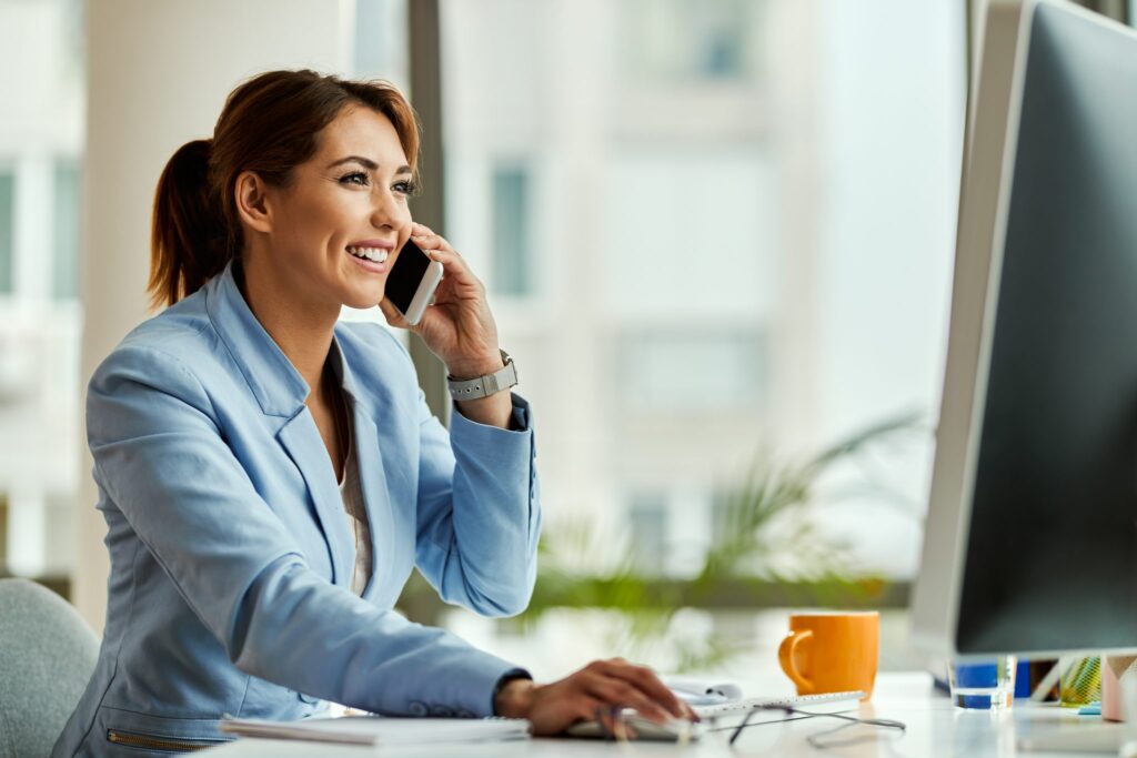 young happy businesswoman working desktop pc communicating mobile phone office